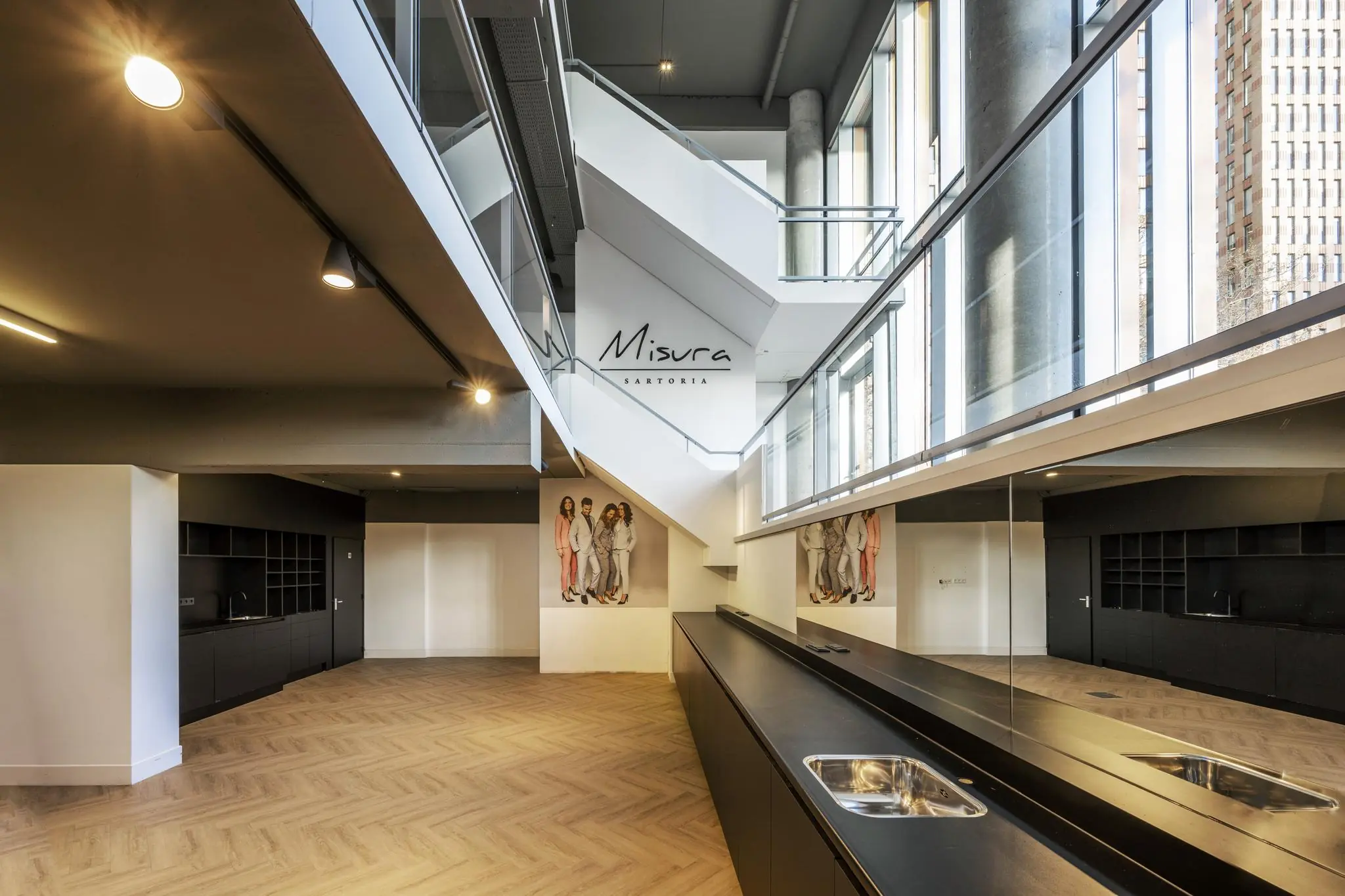 Interieur van een modern kledingatelier aan het George Gershwinplein met een open trap, grote raampartijen en een zwarte keukenunit.